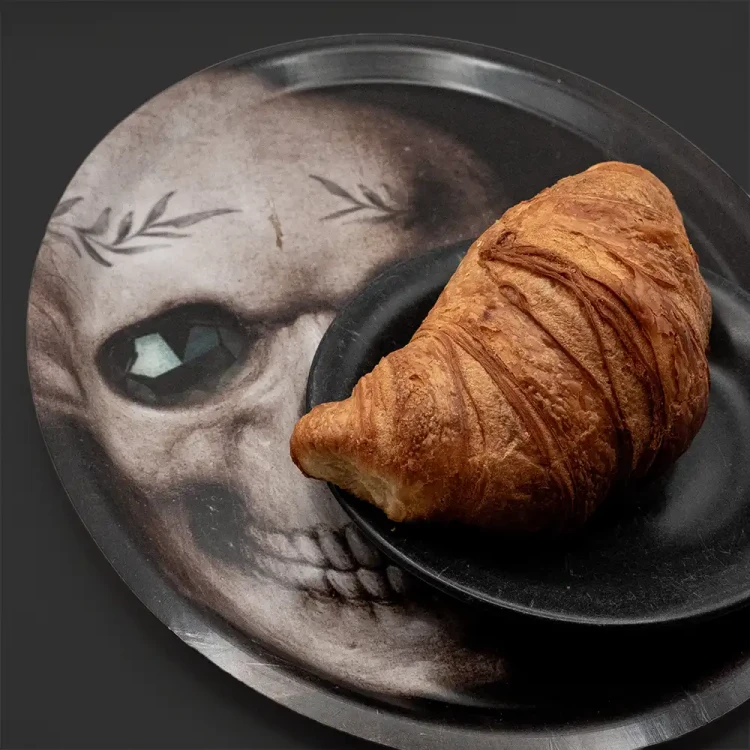 talerzyk z croissantem stojacy na małej owalnej tacy z motywem czaszki